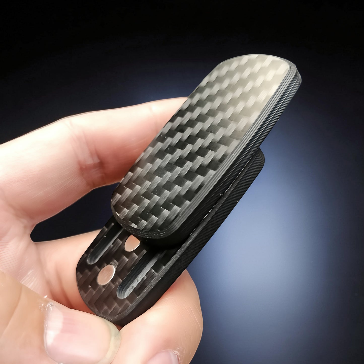 The Curious Mind carbon fiber magnetic slider fidget toy with a black woven pattern, held in a hand.