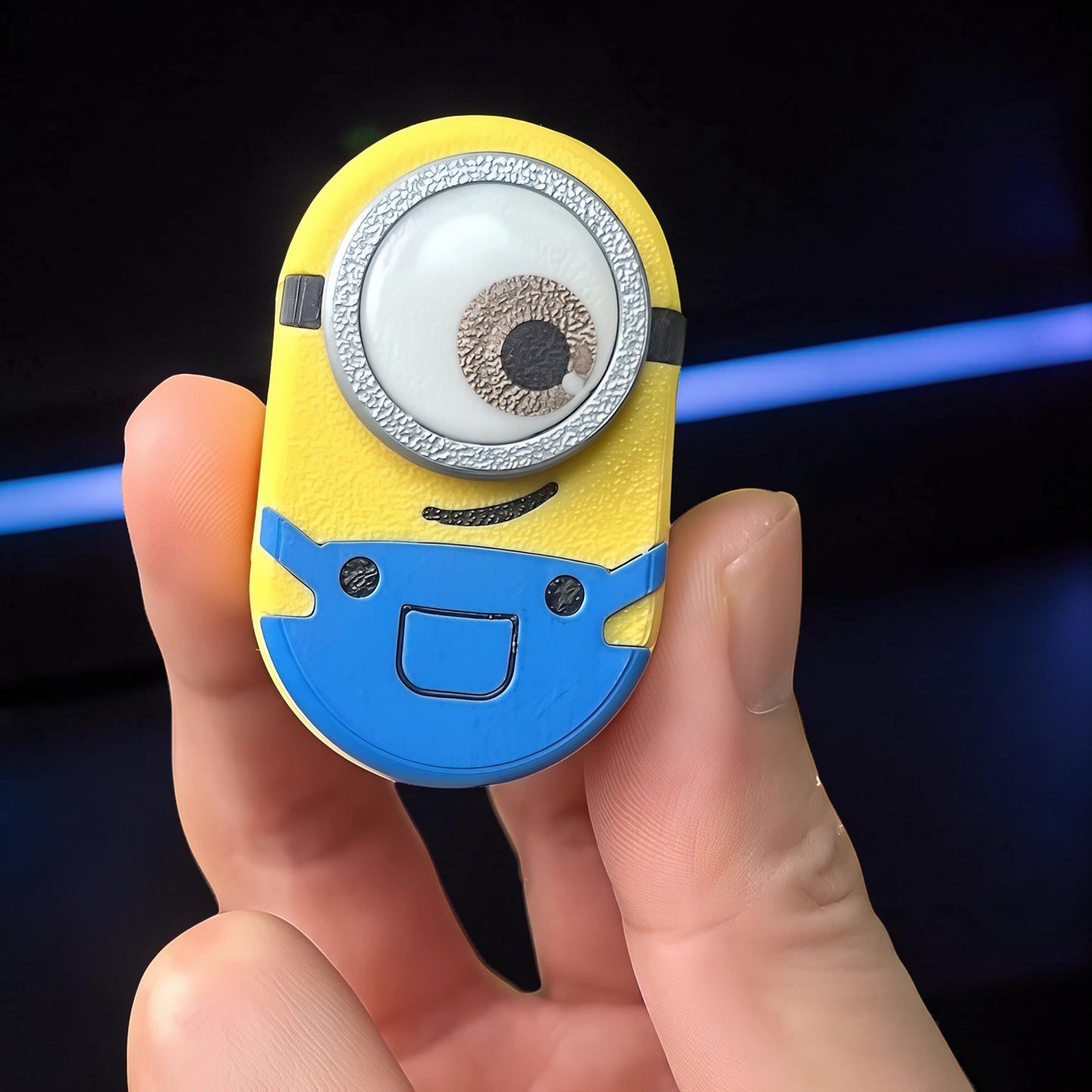 The Curious Mind Minion Pocket Push Pop Clicker fidget toy, yellow and blue metal, with one eye and overalls design.