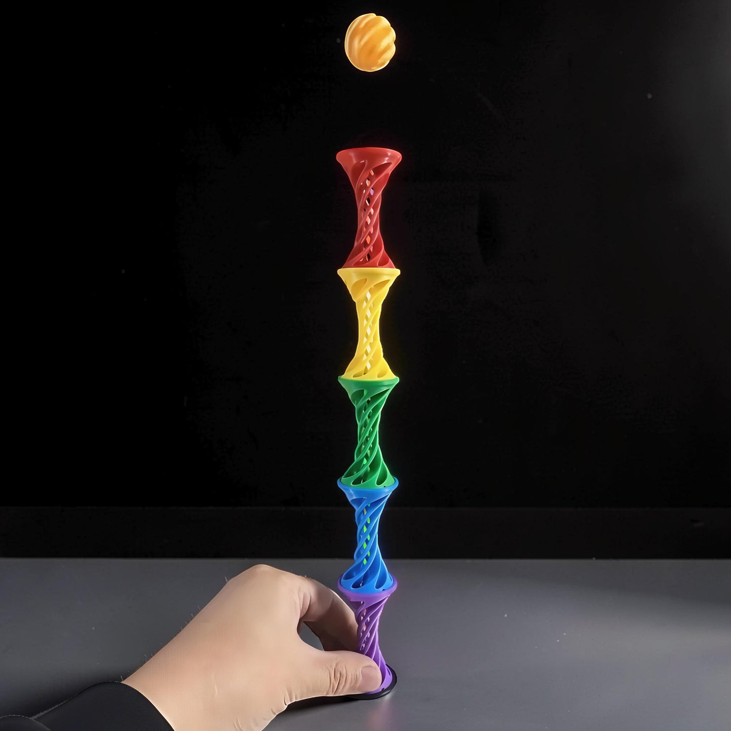 The Curious Mind Rainbow Spiral Ejection Ball fidget toy stacked in rainbow colors, with a yellow ball mid-air.
