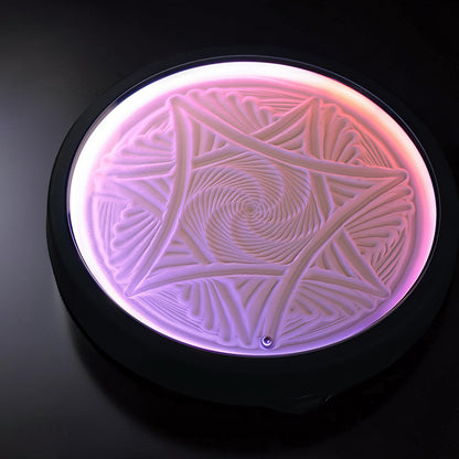 The Curious Mind Kinetic Sand Painting Machine, 20cm, with intricate swirling patterns in white sand illuminated by pink and purple light.