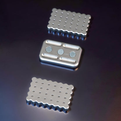 The Curious Mind Biscuit Push Card Slider fidget toy, made of silver metal with a scalloped edge and textured surface.