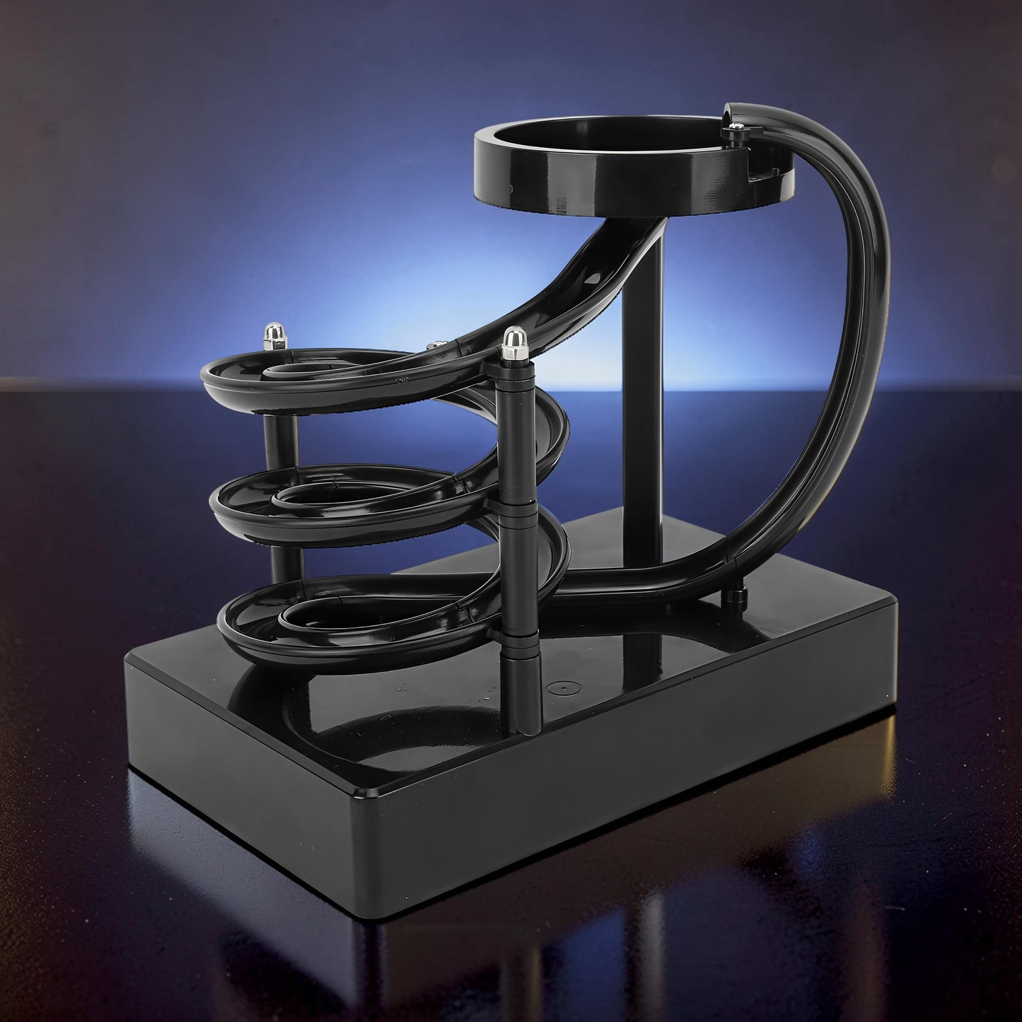 The Curious Mind black electromagnetic perpetual motion machine with a spiral track and metal balls on a reflective surface.