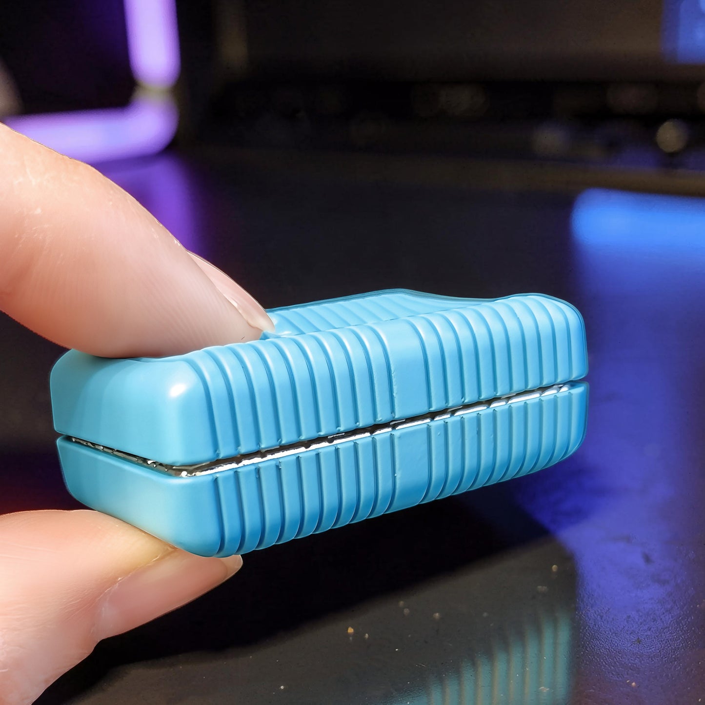The Curious Mind blue magnetic slider fidget toy with ribbed texture, held between fingers.