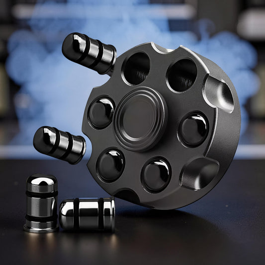 The Curious Mind Brass Finger Gyro Spinner, shaped like a revolver cylinder with bullet-shaped weights. Dark grey metal.