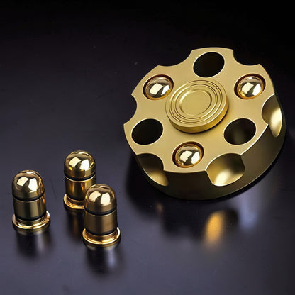 The Curious Mind Brass Finger Gyro Spinner with bullet-shaped weights. This metal fidget toy has a revolver cylinder design and a gold finish.