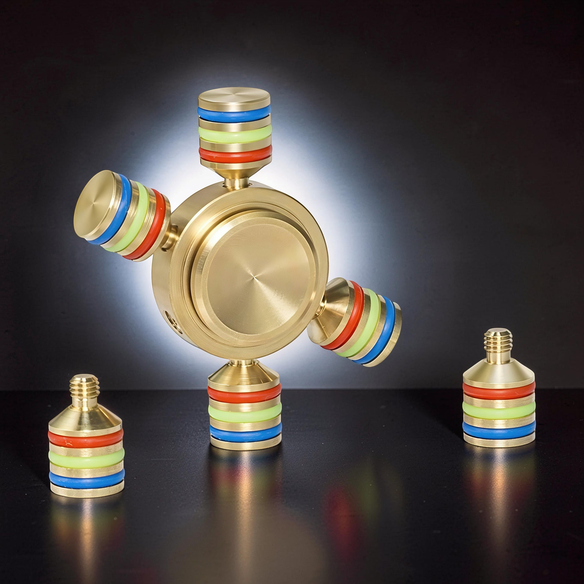 The Curious Mind brass tri-spinner fidget toy with red, green, and blue bands on arms and base.