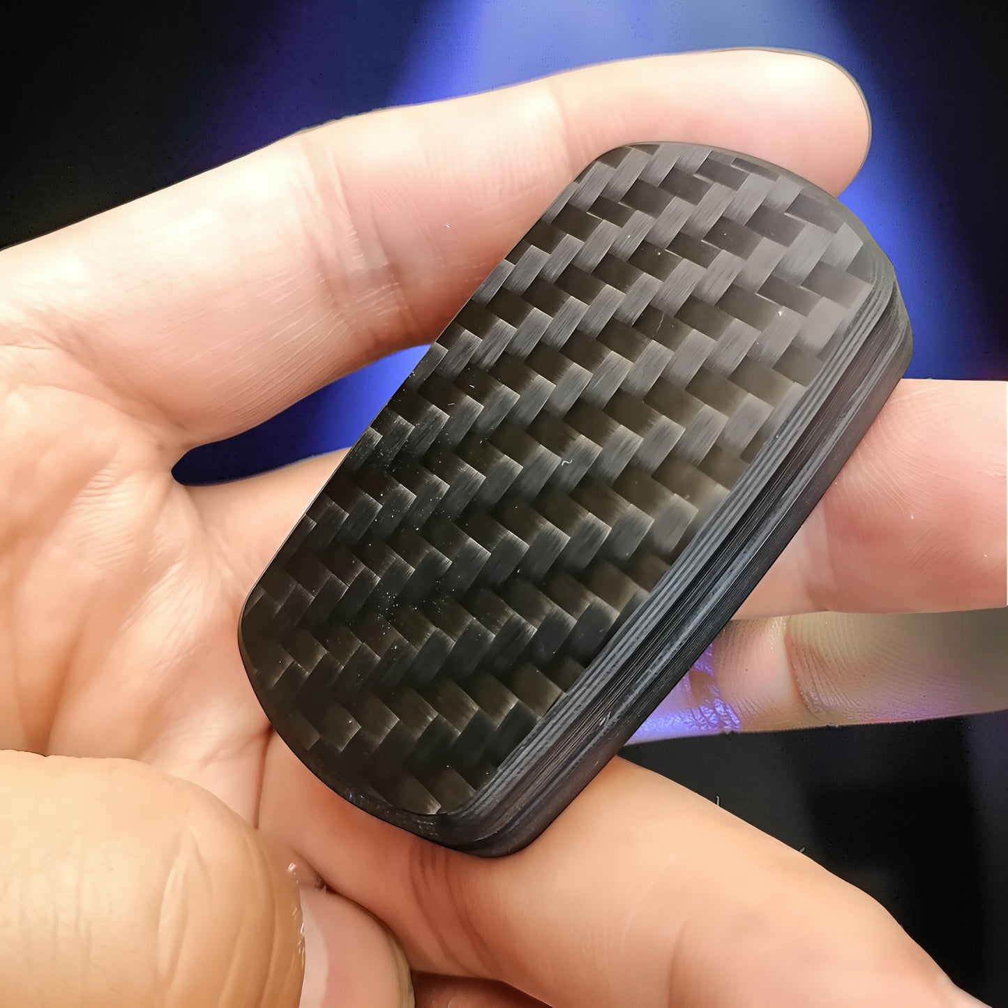 The Curious Mind carbon fiber magnetic slider fidget toy with a woven black pattern, held in a hand.