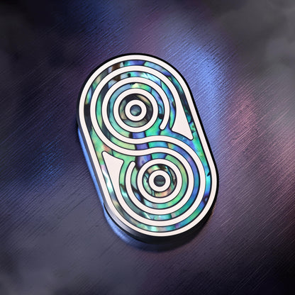 The Curious Mind Fritillary Push Slider fidget toy with a metallic silver frame and iridescent abalone shell inlay in a yin-yang design.