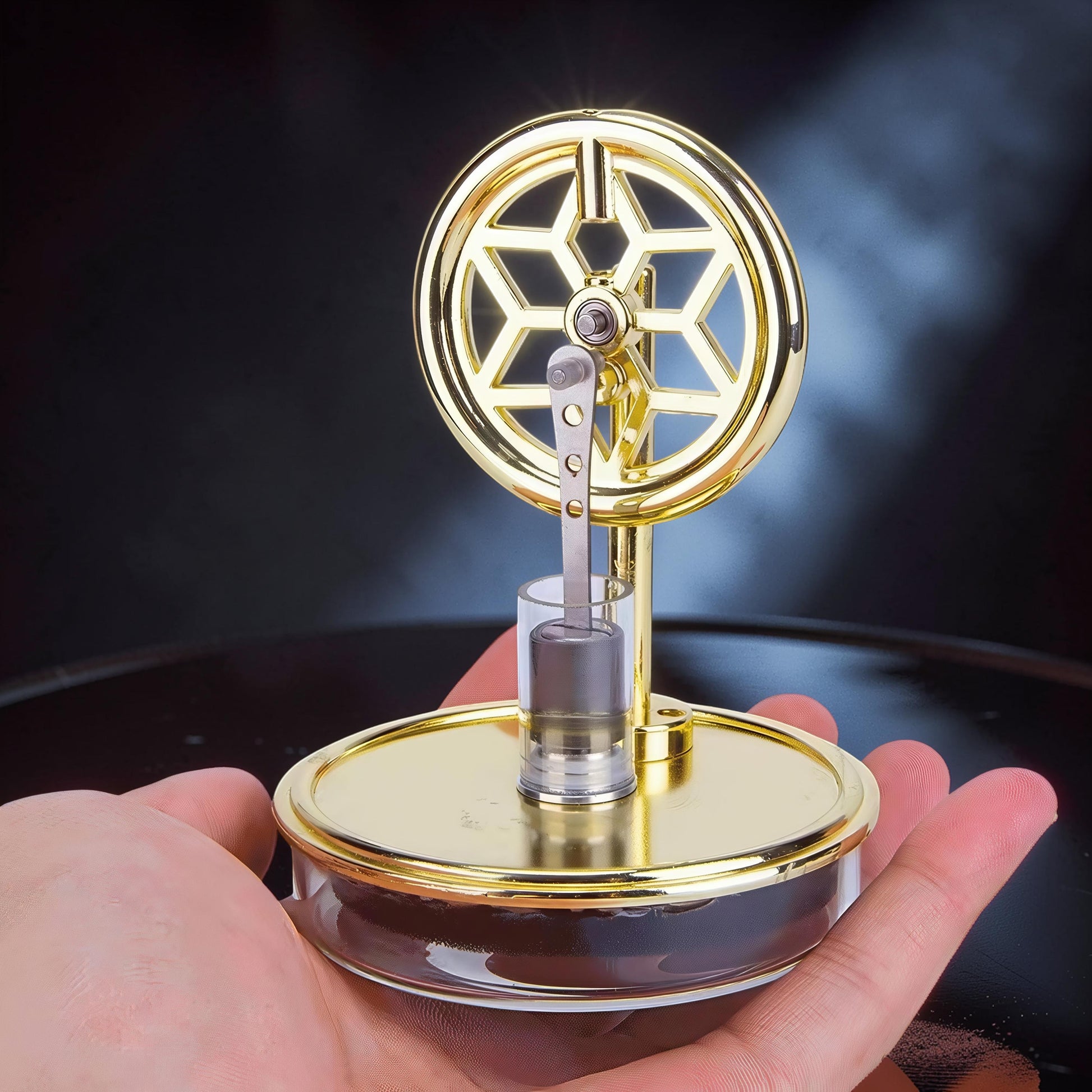 The Curious Mind gold metal Stirling engine display model with decorative flywheel and glass cylinder.