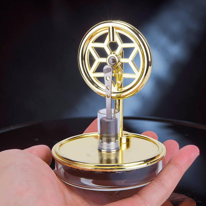 The Curious Mind gold metal Stirling engine display model with decorative flywheel and glass cylinder.