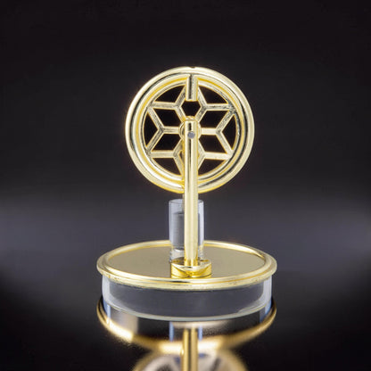 The Curious Mind gold metal Stirling engine display model with a snowflake-like flywheel on a clear acrylic base.