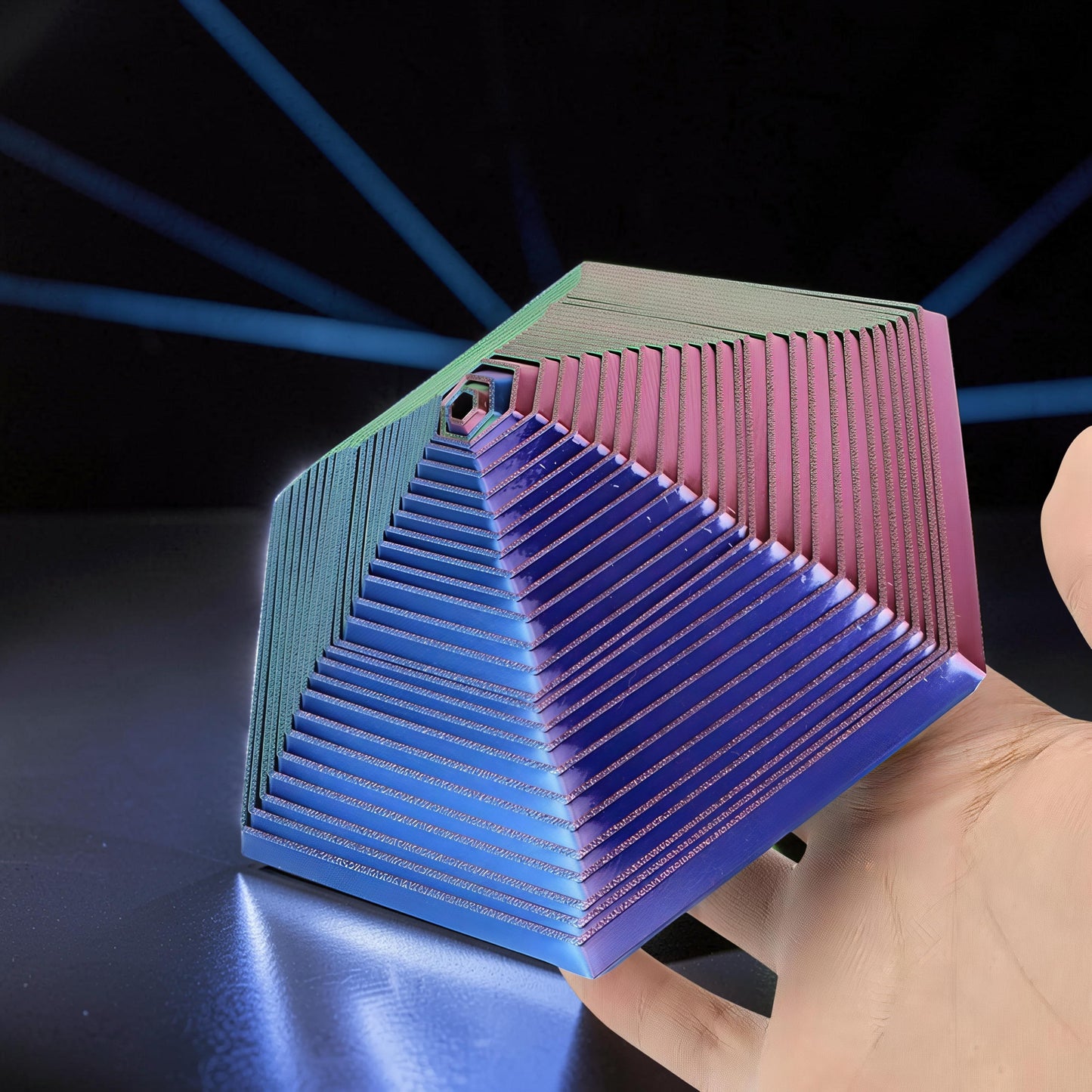 The Curious Mind Hexagon Push Fidget sensory toy in blue, pink, and green PLA, held in a hand.