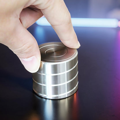 The Curious Mind Vortecon kinetic desk spinner, a weighted silver metal cylinder with horizontal grooves, being spun by a finger.