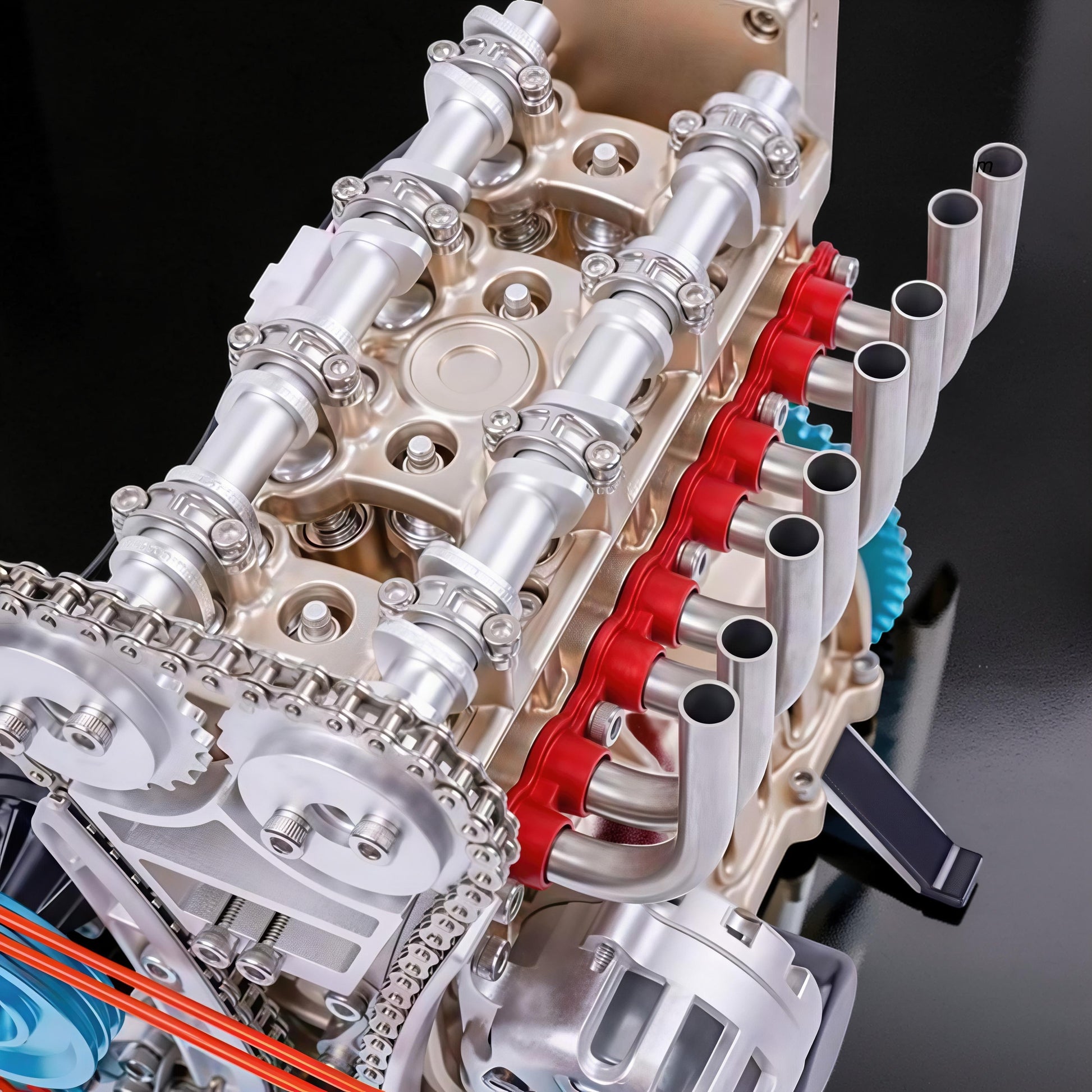 The Curious Mind L4 four-cylinder engine model kit, made of metal, with silver and gold accents, red detailing, and visible gears and chain.
