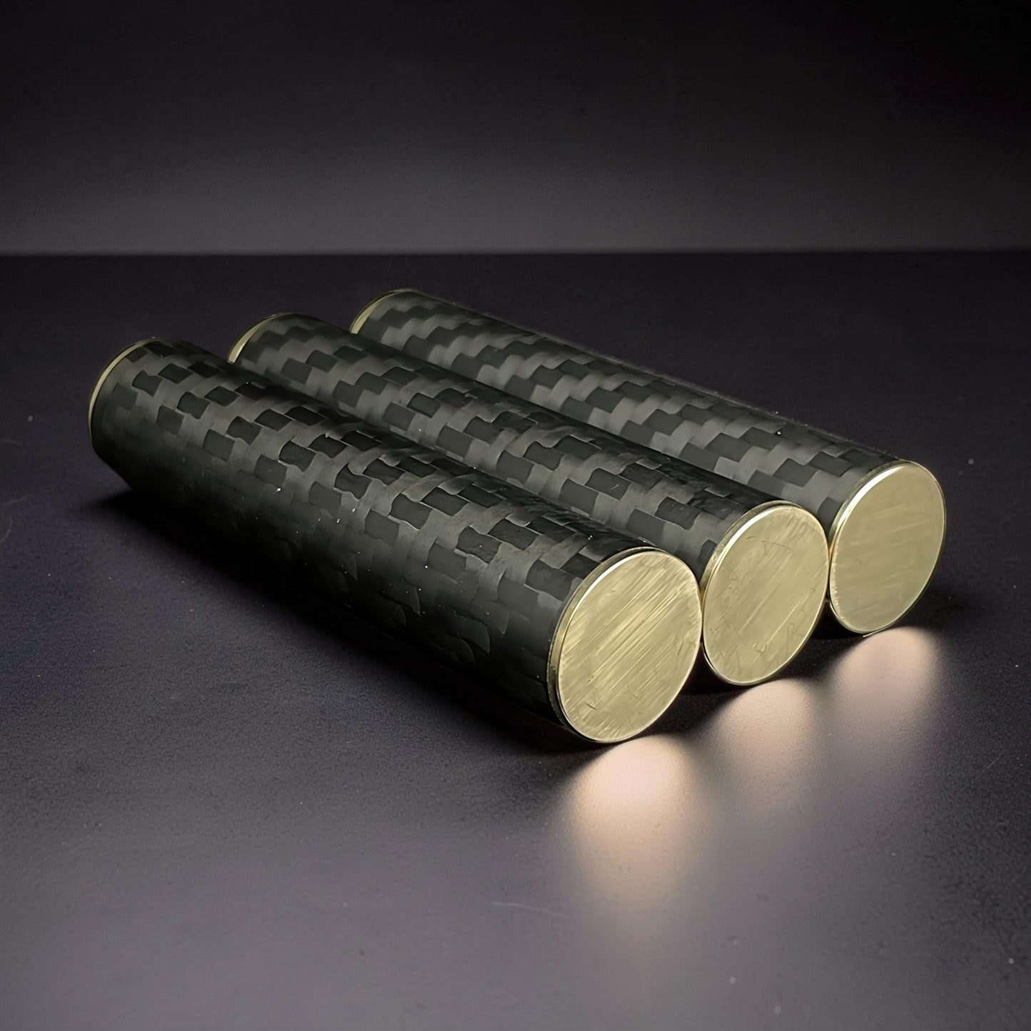 The Curious Mind Magnetic Carbon Fiber Slider with brass ends. Three cylindrical fidget toys with a woven carbon fiber pattern.