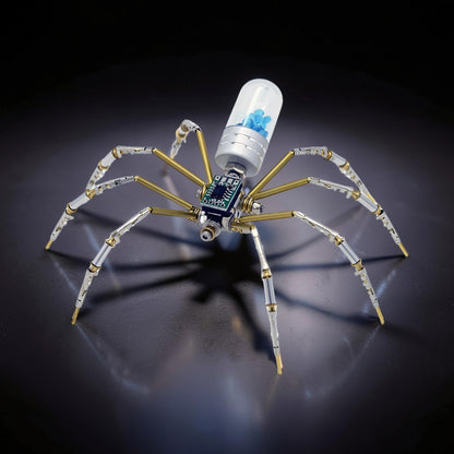The Curious Mind Style B mechanical spider model kit, made of metal with brass accents and a clear capsule containing blue beads.