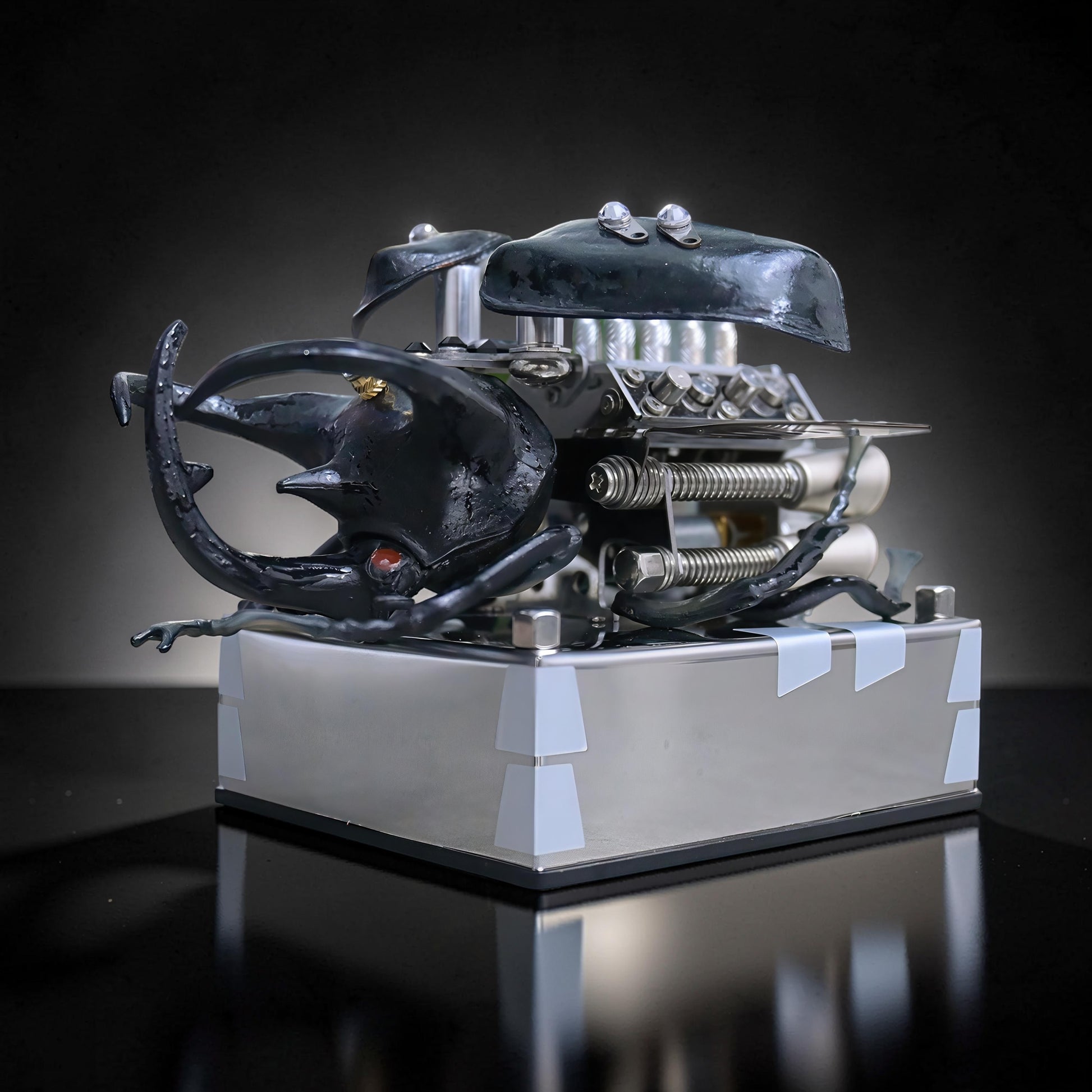 The Curious Mind Mechanical V8 Beetle Display Model, a black alloy metal and resin sculpture with intricate mechanical details, on a silver base.