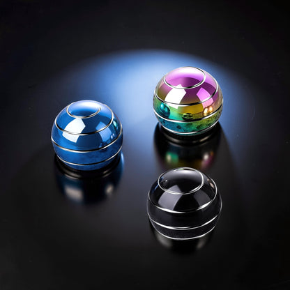 The Curious Mind high-gloss metal desktop stress ball in blue, iridescent, and black finishes. Weighted fidget toy for desk.