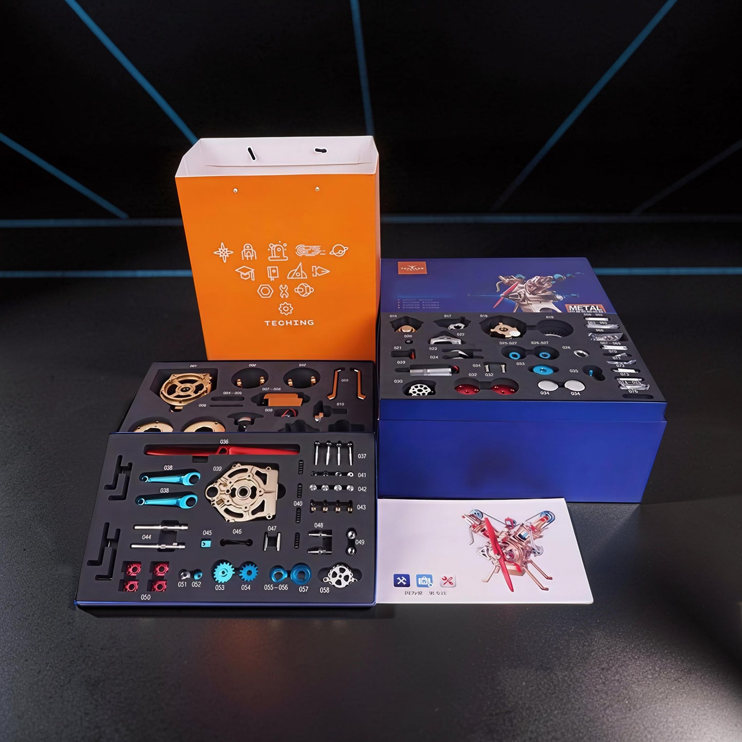 The Curious Mind Mini V2 Double-Cylinder Engine DIY Kit with metal parts laid out in foam organizers, plus packaging and instructions.