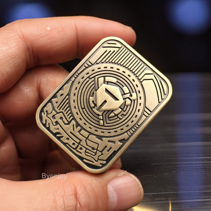 The Curious Mind Three-Body Push Card Fidget, a compact metal clicker with intricate circuit board design and a central geometric emblem. Antique brass finish.