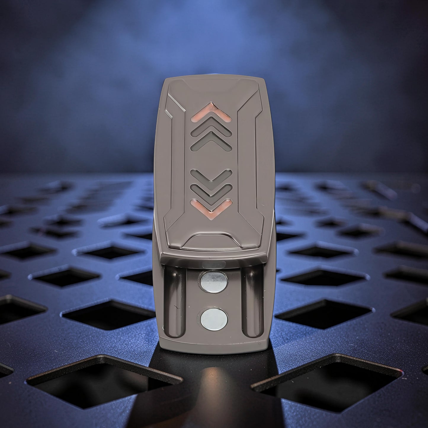 The Curious Mind Arrow Pusher Click Slider fidget toy, a compact metal slider with a dark grey finish and orange arrow accents.