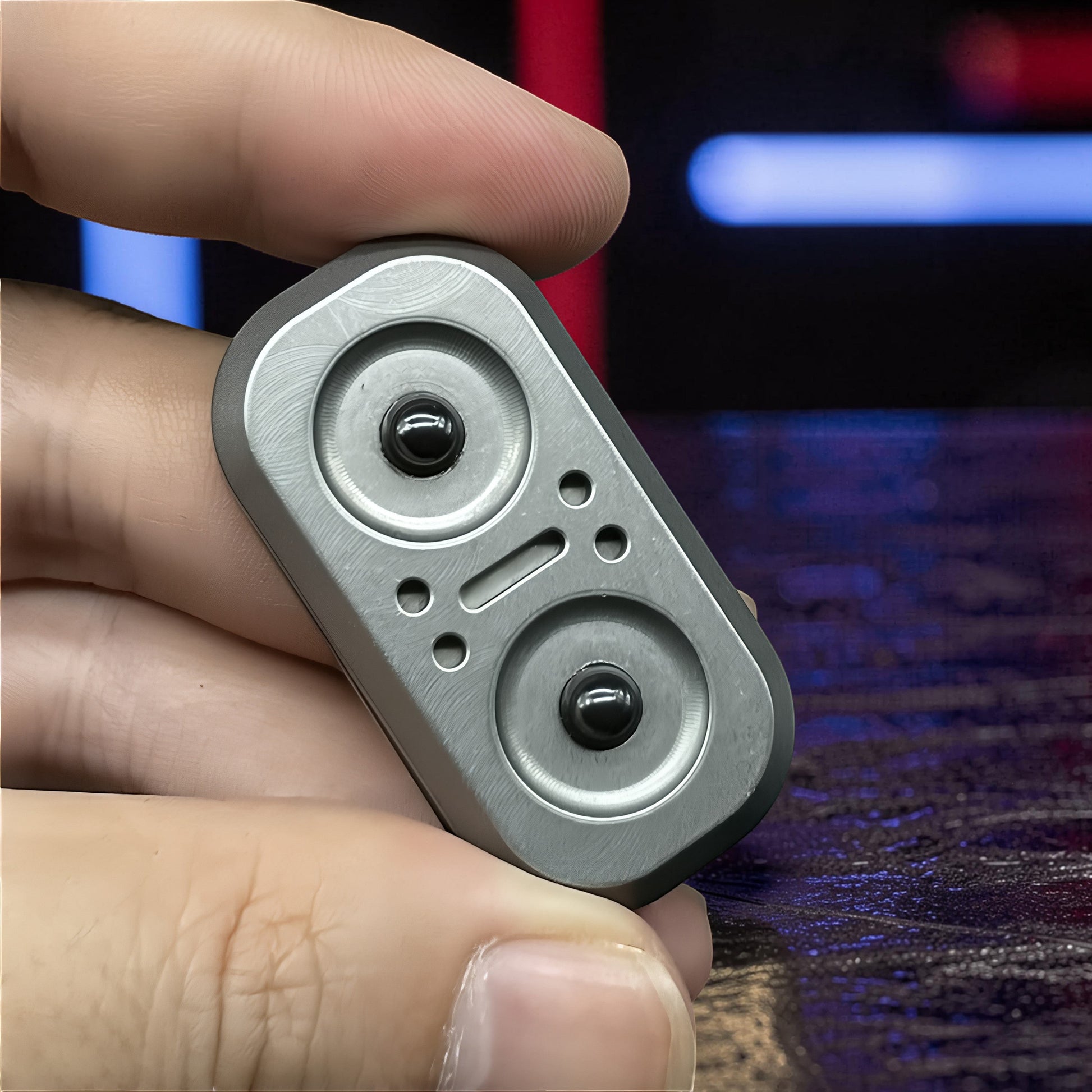 The Curious Mind Owl Push Slider, a compact metal fidget toy with a brushed silver finish and two black push buttons.
