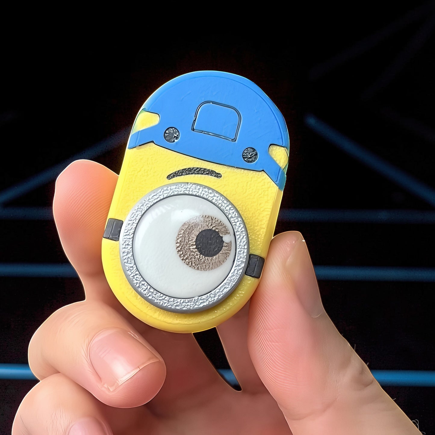 The Curious Mind Minion Pocket Push Pop Clicker fidget toy, yellow and blue metal and plastic, featuring a large eye.