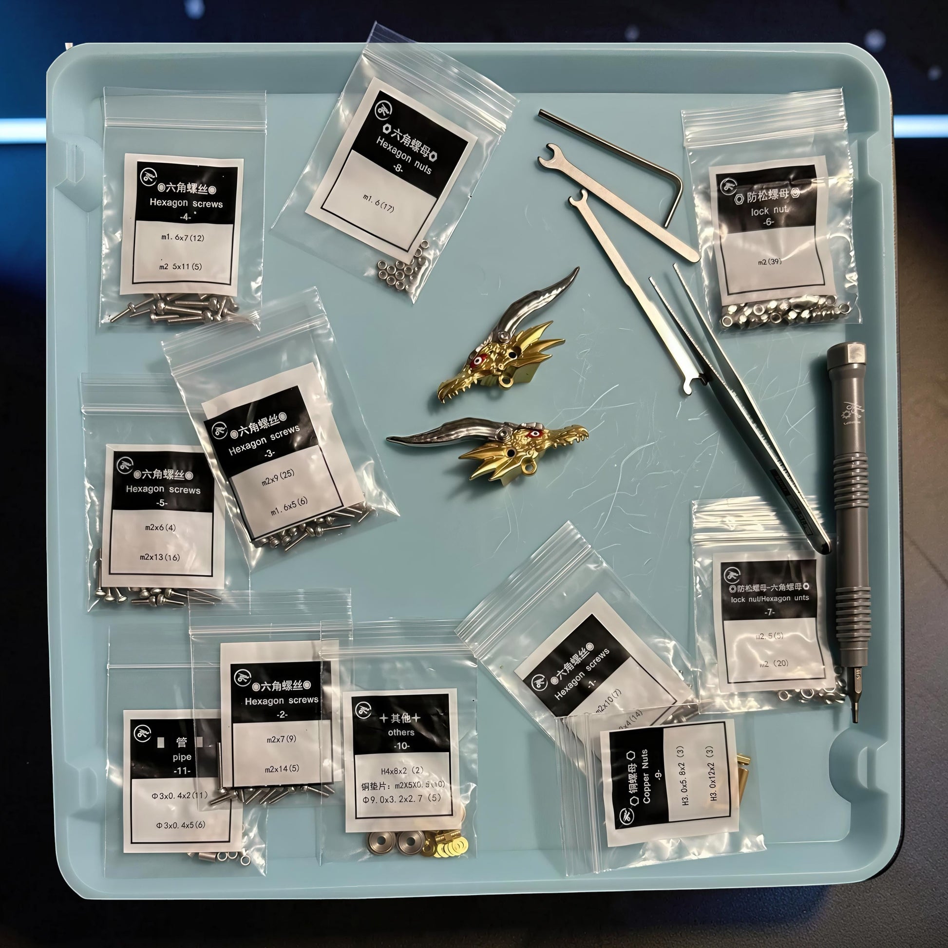 The Curious Mind Pterosaur DIY Kit includes metal parts, screws, nuts, tools, and decorative dragon heads for a mechanical creature model.