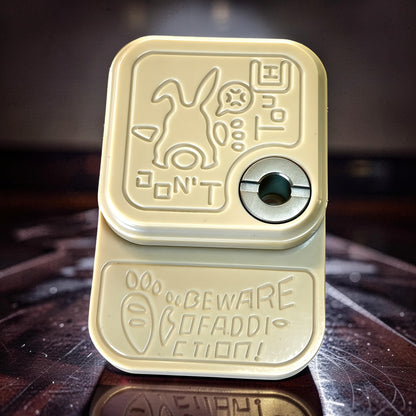 The Curious Mind Rabbit Side-Press Clicker fidget toy in cream metal with engraved rabbit and 'Don't Touch' text. Features a central click mechanism.