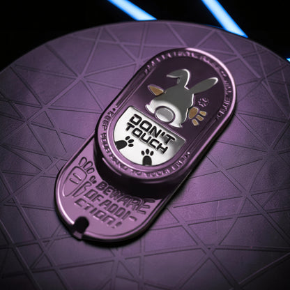 The Curious Mind Don't Touch Rabbit Slider: a purple metal fidget toy with a rabbit graphic and paw prints. Features tactile sliding action.