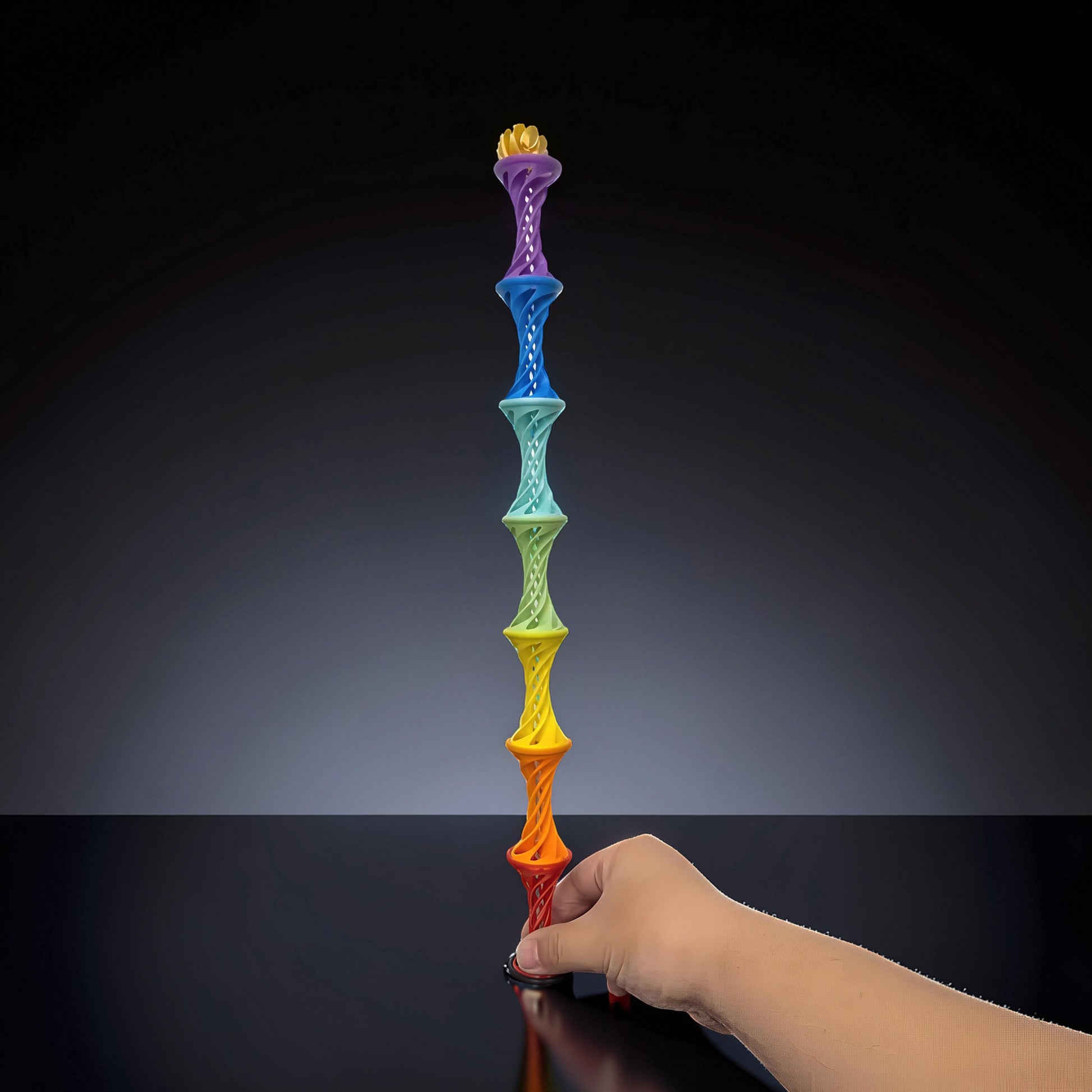 The Curious Mind Rainbow Spiral Ejection Ball fidget toy stacked high, held by a hand. Made of PLA.