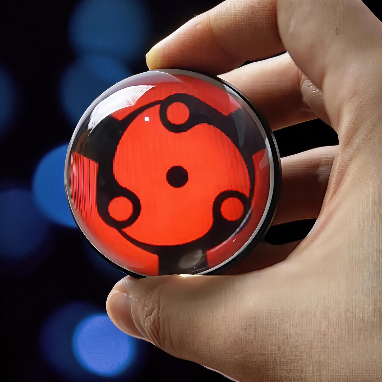 The Curious Mind Sharingan Crystal Ball Decorative Ornament, a red and black orb with concentric circles, held in a hand.