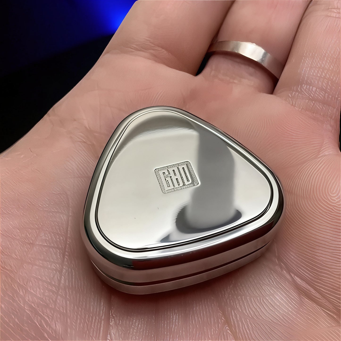 The Curious Mind silver metal rice ball push card fidget slider with GRID logo on top, held in a palm.