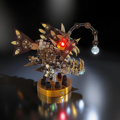 The Curious Mind Steampunk Anglerfish metal model kit with display base, featuring intricate gears, a red light-up eye, and a glowing lure.