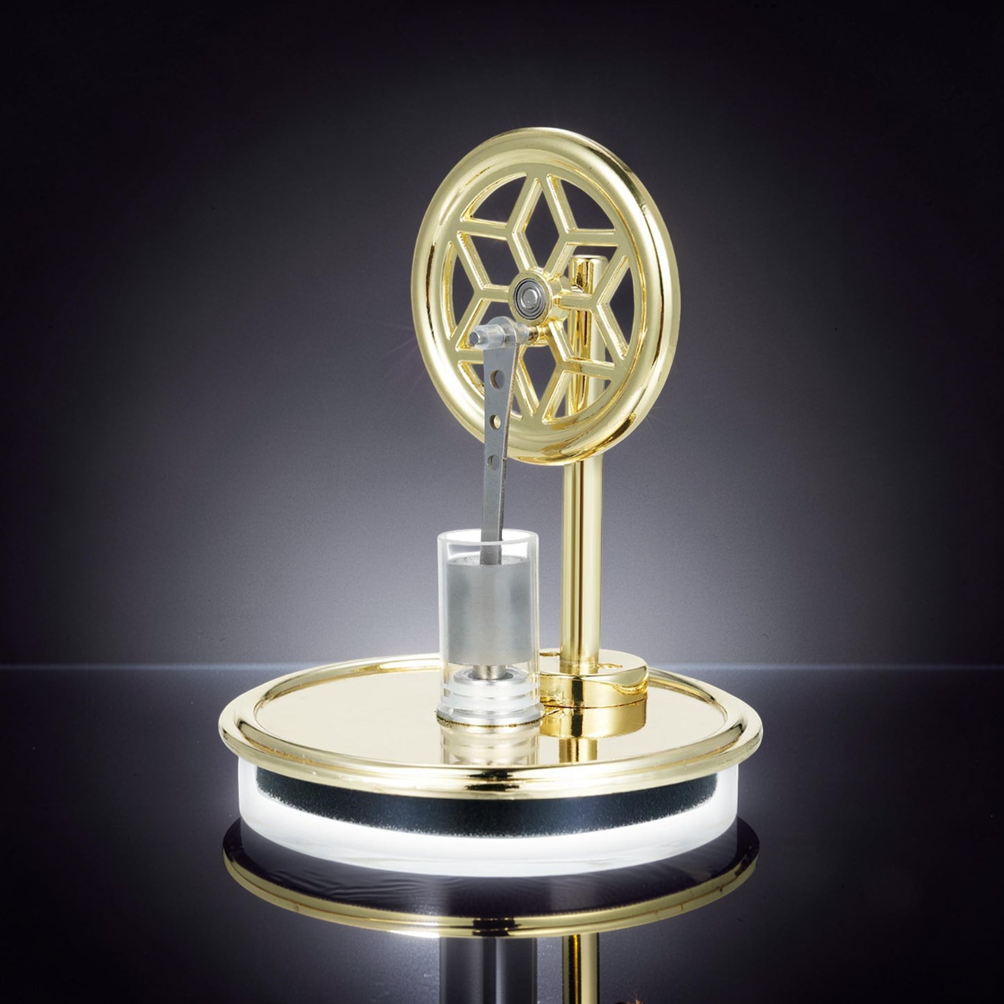 The Curious Mind Temperature Difference Stirling Engine Display Model, a polished gold metal engine with a decorative flywheel and clear cylinder on a reflective base.