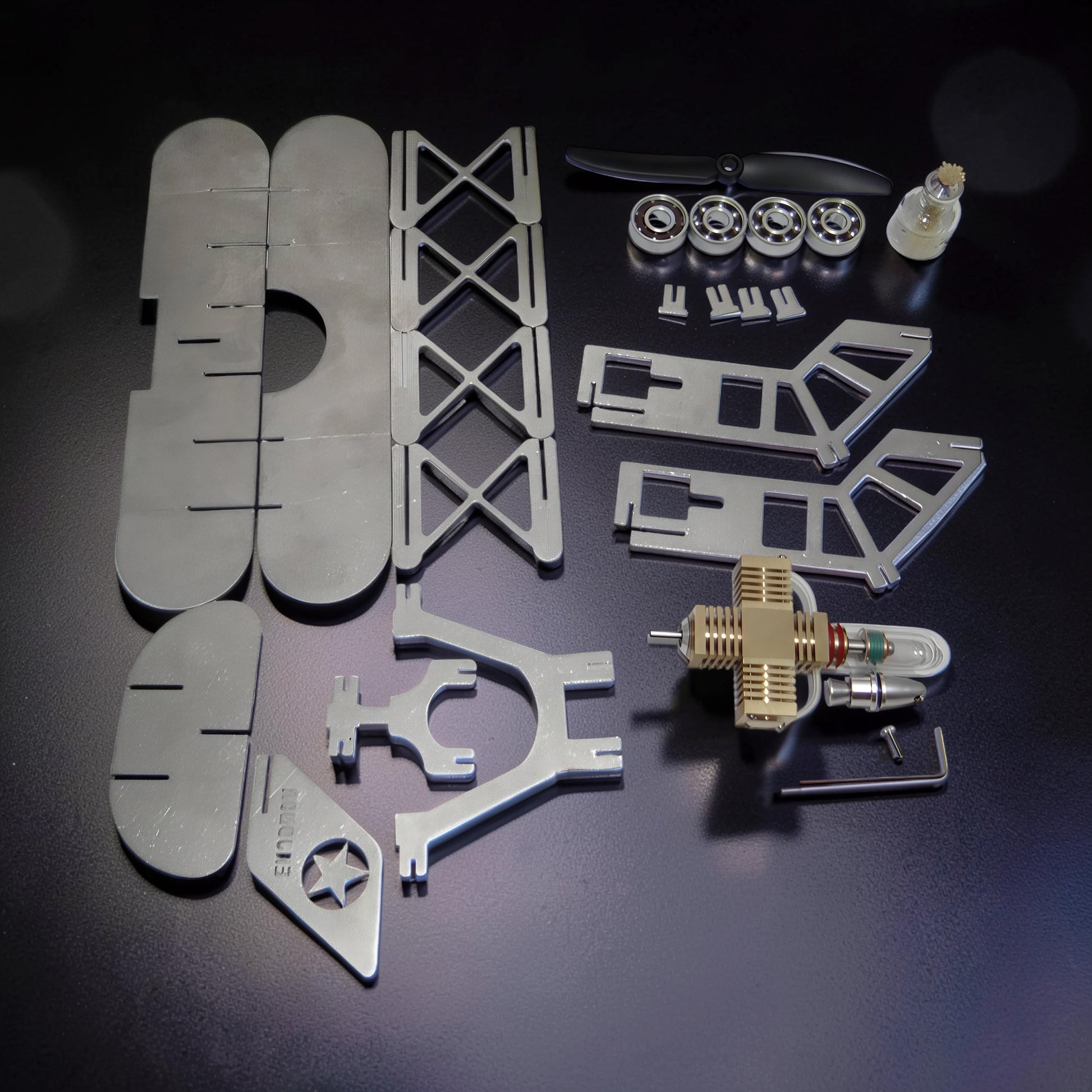 The Curious Mind Stirling Engine Model Aircraft kit with metal parts, engine, propeller, and bearings on a dark surface.