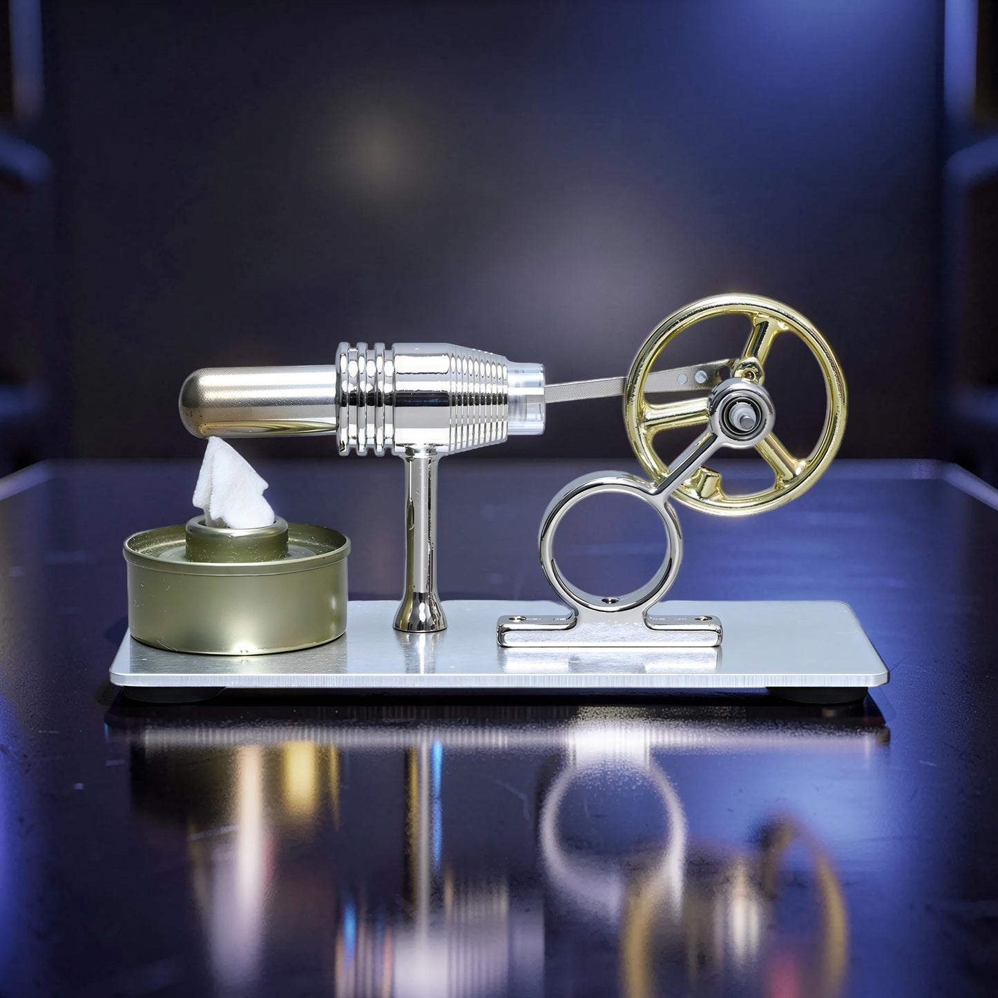 The Curious Mind Classic Stirling engine model with gold flywheel and silver metal body on a reflective surface.