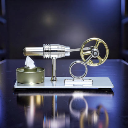 The Curious Mind Classic Stirling engine model with gold flywheel and silver metal body on a reflective surface.