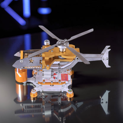 The Curious Mind Fire-Absorbing Stirling Helicopter Model, a metal engine display with gold and silver accents, featuring spinning rotors and a star detail.