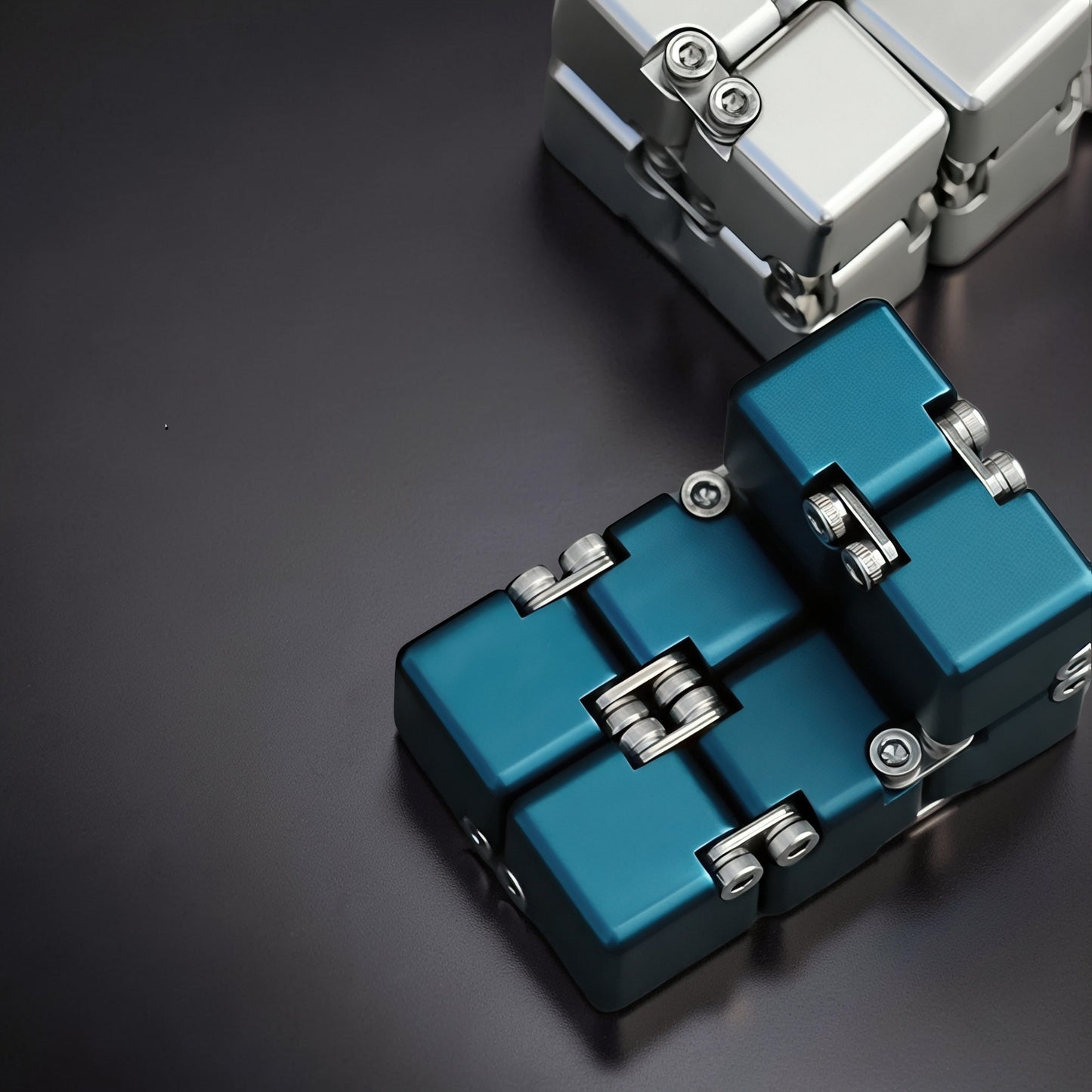 The Curious Mind Unlimited Magic Fidget Cube in teal metal with silver accents, a compact desk toy for focus and stress relief.
