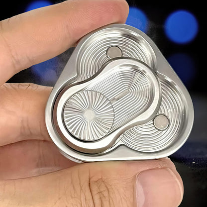 The Curious Mind Triangle Rotary Push Card fidget toy, made of brushed metal with intricate grooved patterns and magnetic sliders.