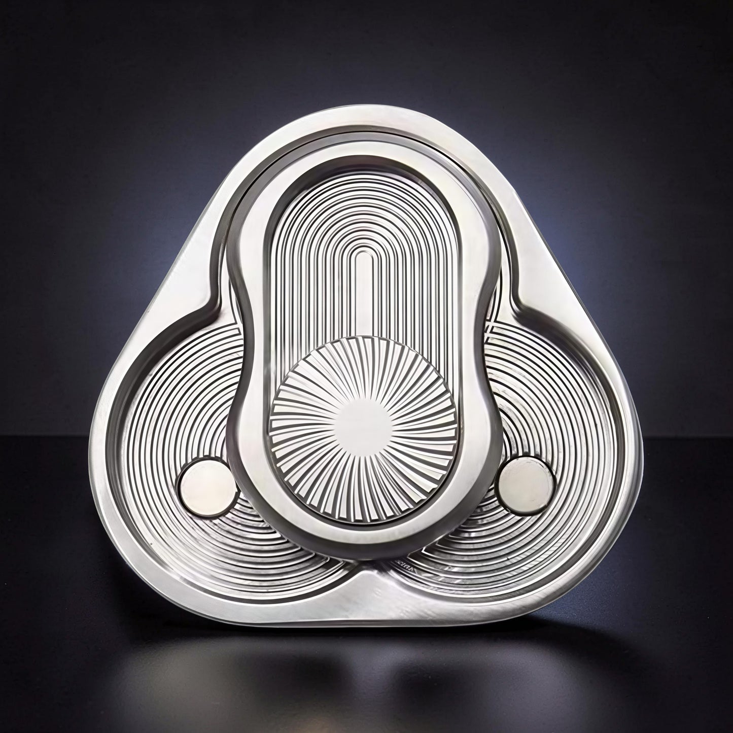 The Curious Mind triangle rotary push card fidget toy, made of silver metal with intricate concentric circle and sunburst patterns.