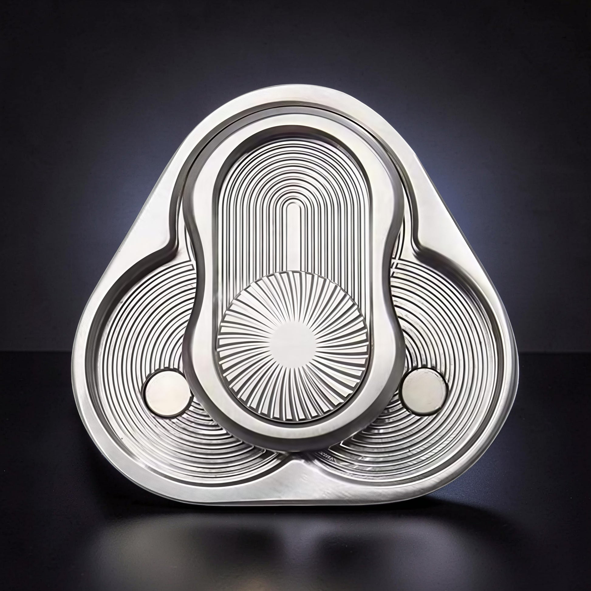 The Curious Mind triangle rotary push card fidget toy, made of silver metal with intricate concentric circle and sunburst patterns.