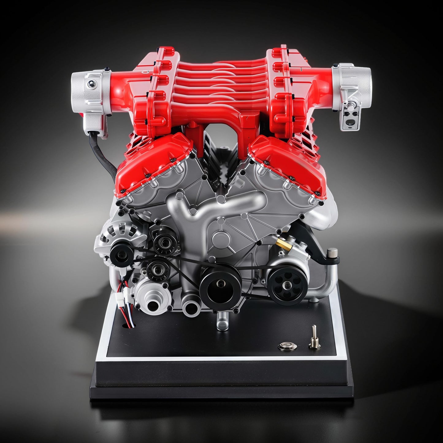 The Curious Mind V12 Car Engine DIY Kit, a detailed metal model with red and silver components, mounted on a black display base.