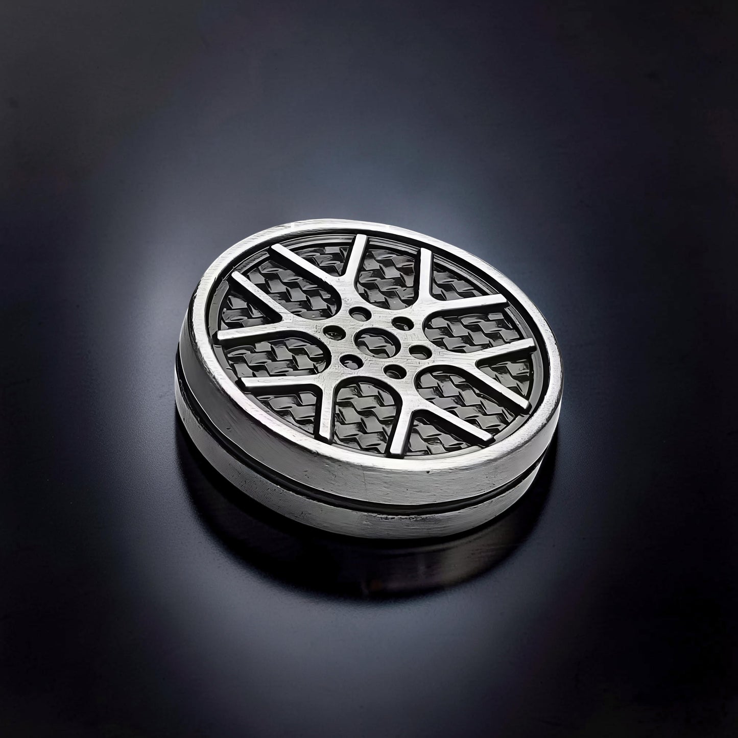 The Curious Mind Wheel Hub Coin Clicker fidget toy with a silver metal rim and a black carbon fiber pattern wheel design.