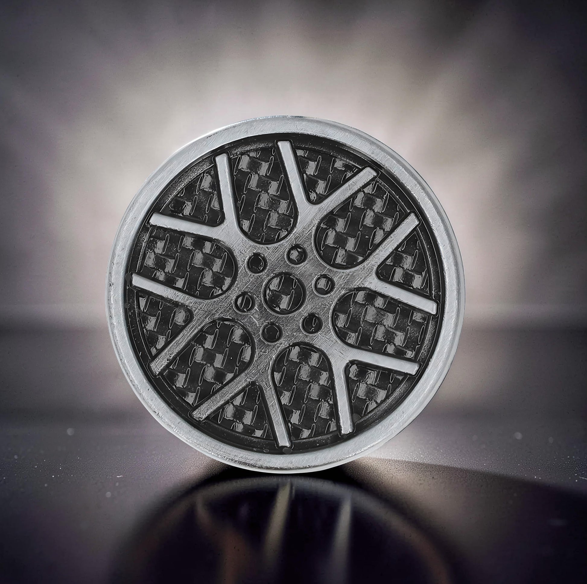 The Curious Mind Wheel Hub Coin Clicker fidget toy with a metal alloy construction and carbon fiber pattern.