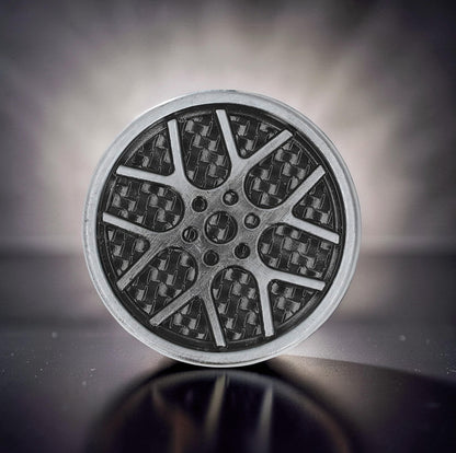 The Curious Mind Wheel Hub Coin Clicker fidget toy with a metal alloy construction and carbon fiber pattern.