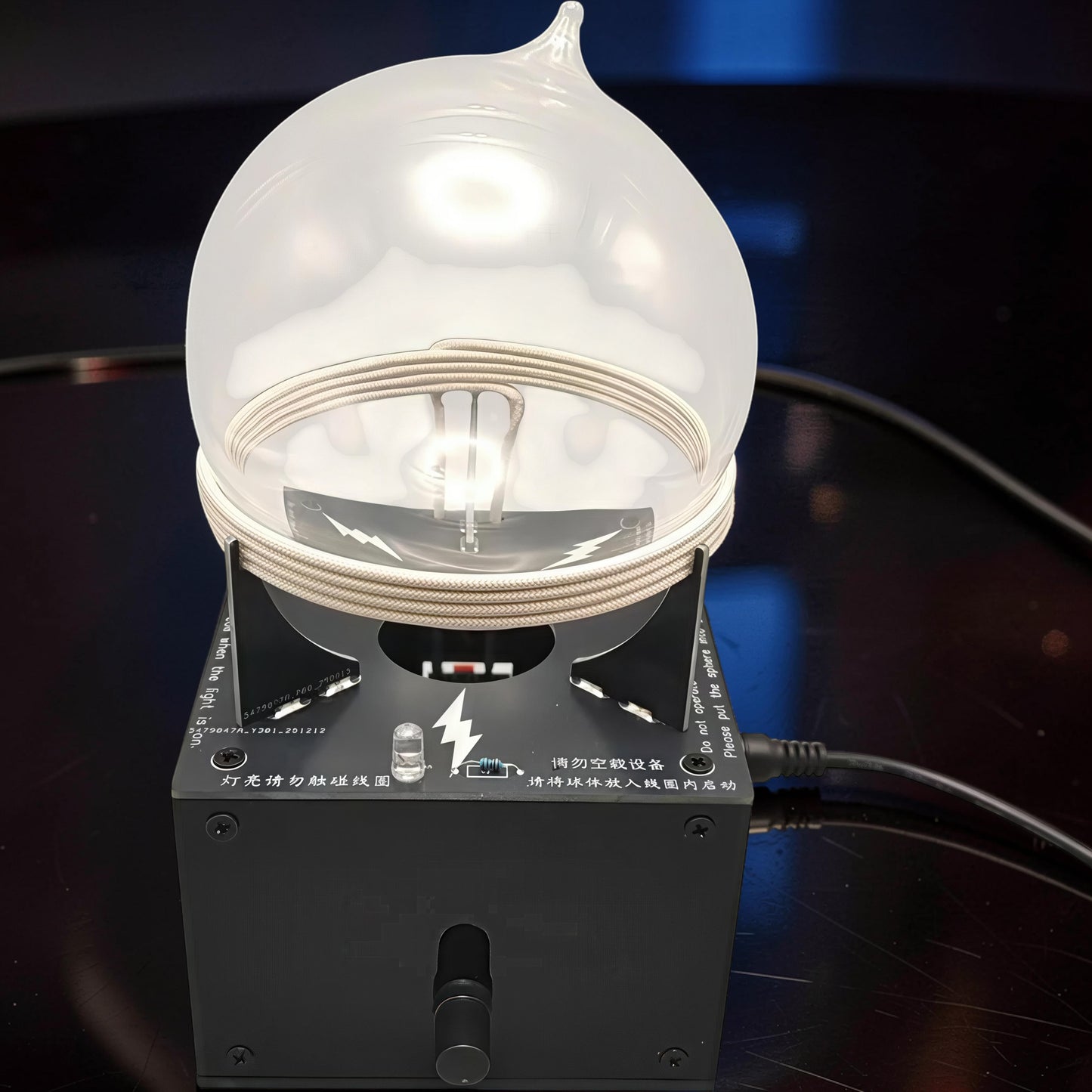 The Curious Mind Xenon Ion Ring Glass Sphere, an interactive science display with a clear glass globe and internal coil, illuminated by a bright light.