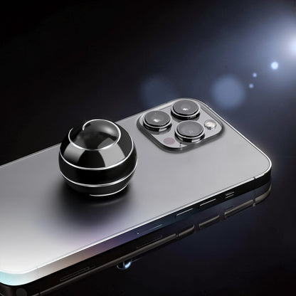 The Curious Mind high-gloss black metal desktop stress ball with silver detailing, shown on a smartphone.