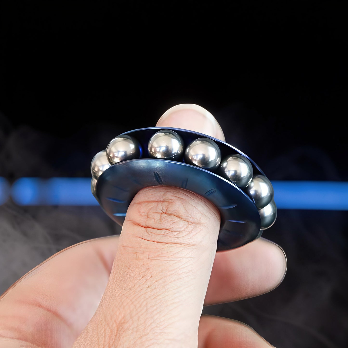 The Curious Mind blue metal bead wheel spinner with silver ball bearings, held on a finger.